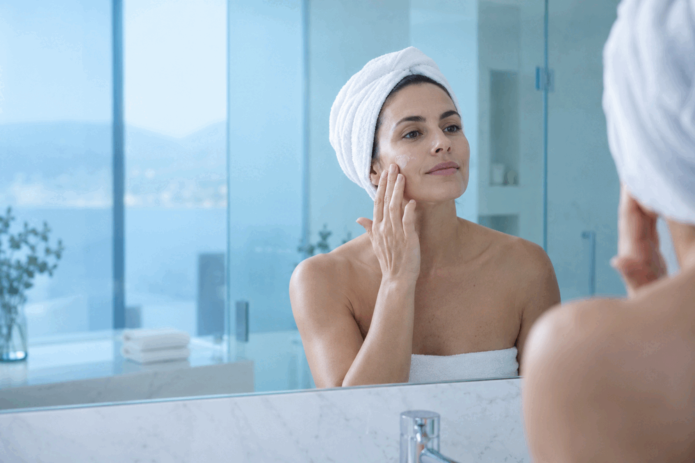 Mujer aplicando crema facial en un entorno luminoso de tonos blancos y azules